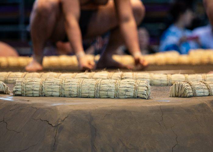 The edges of a sumo wrestling ring. In the background, sumo wrestlers are squatting.